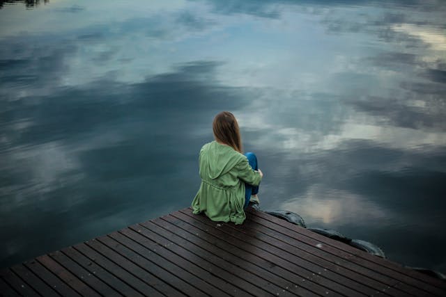 A woman sitting by a body of water.