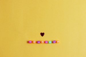 Colorful letter blocks spelling out “YOURSELF” with a small heart on a yellow background