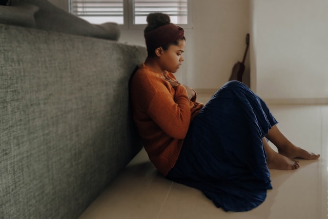 A woman sitting on the floor with a blanket, next to a sofa.