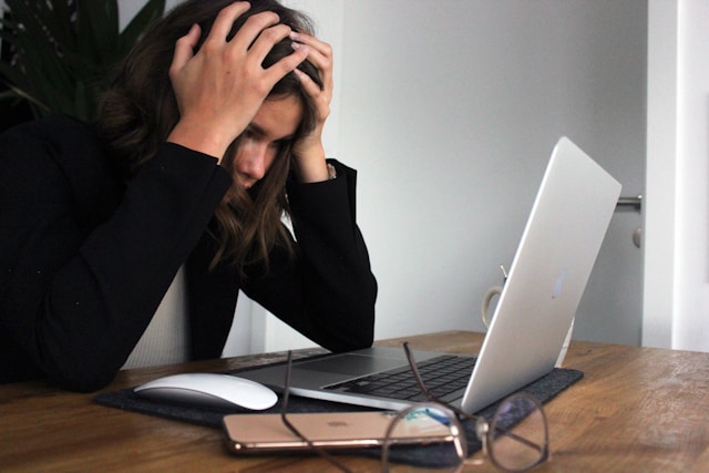 A woman holding her head and looking stressed in front of her laptop.